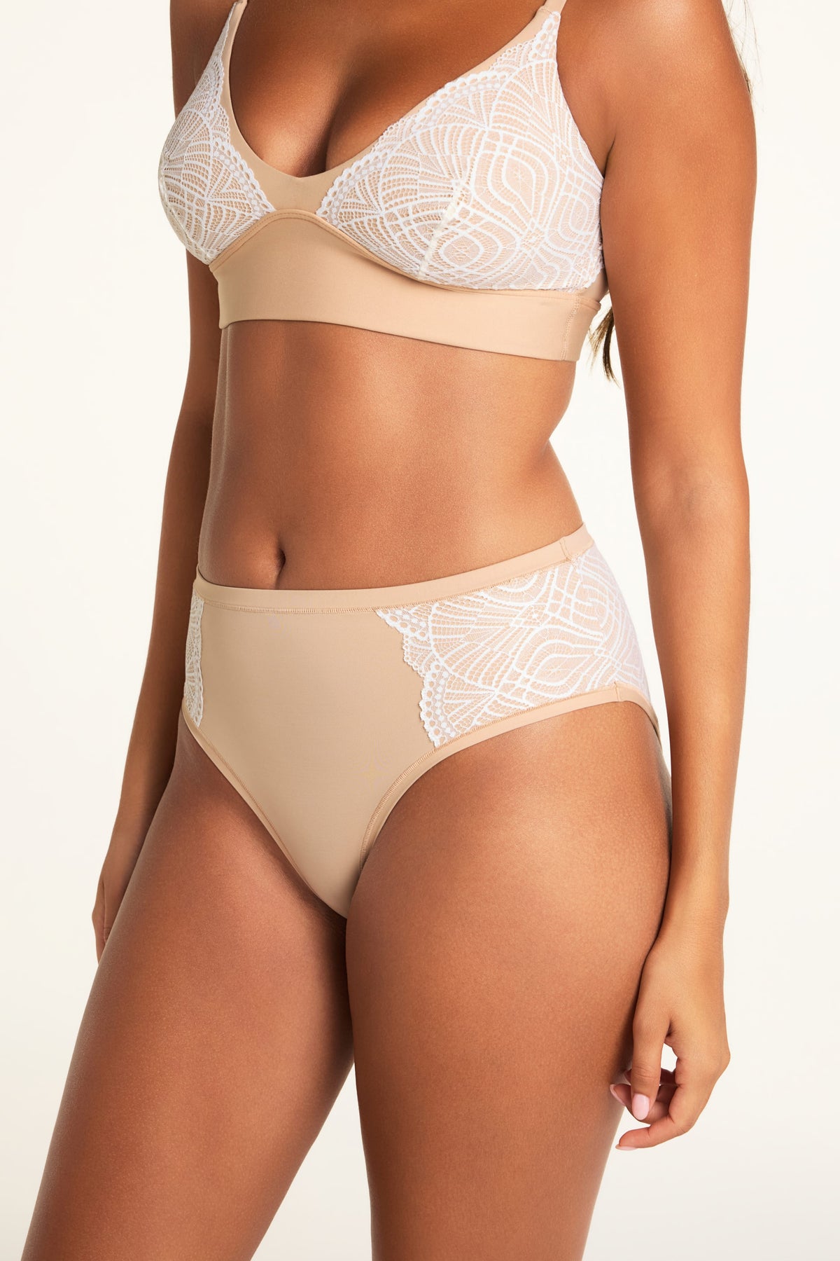 In a bright studio, Kushi wears the Bliss Lace Bralette and Bliss Lace Highwaist Brief in Beige, with a close-up view of the brief’s high waist and white lace panels.