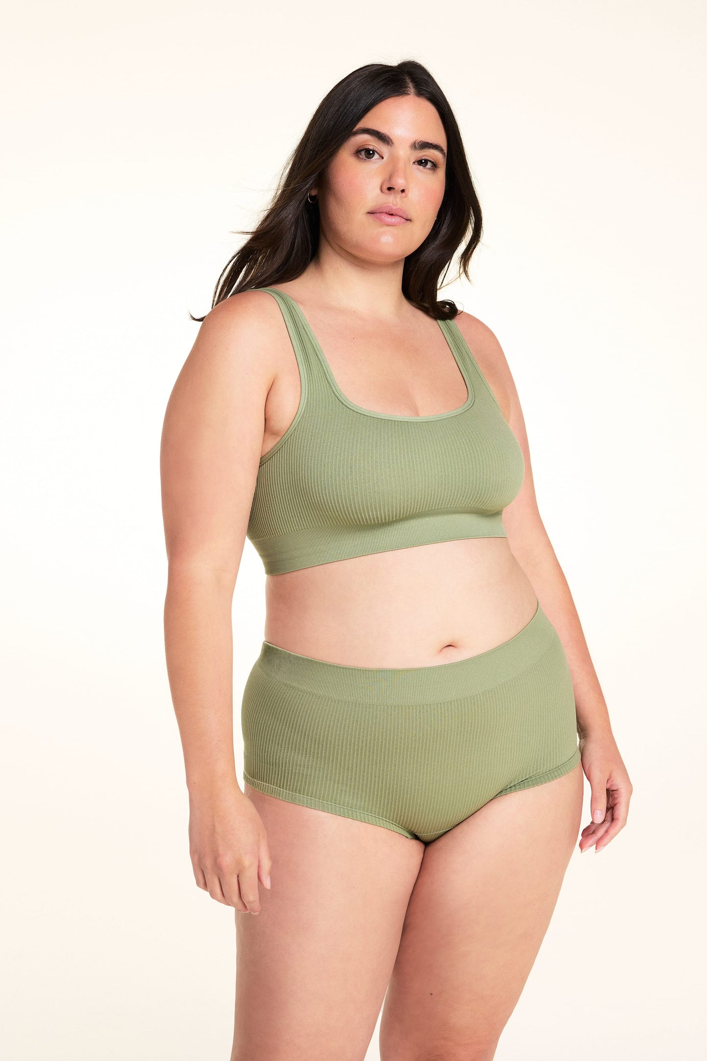 On a white studio backdrop, Alessandra wears the Lounge Rib Sleepshort in Dill with the matching Lounge Rib bralette, showing the ribbed fabric, scoop neckline, and comfortable waistband.