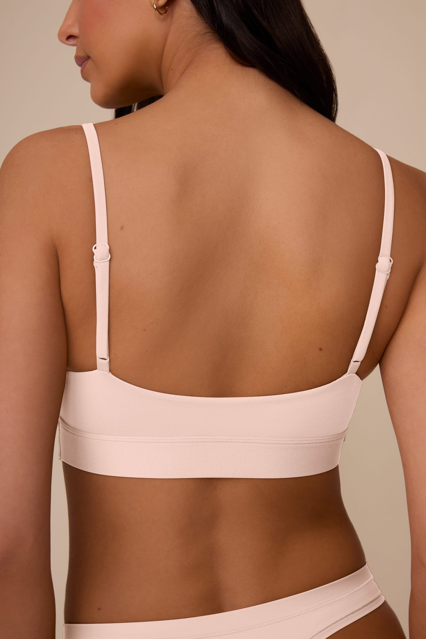 On a neutral beige backdrop, a close-up of Sonnie wearing the Bliss Scoop Adjustable Bralette in Rose highlights the scoop neckline, adjustable straps, and smooth, wireless design.
