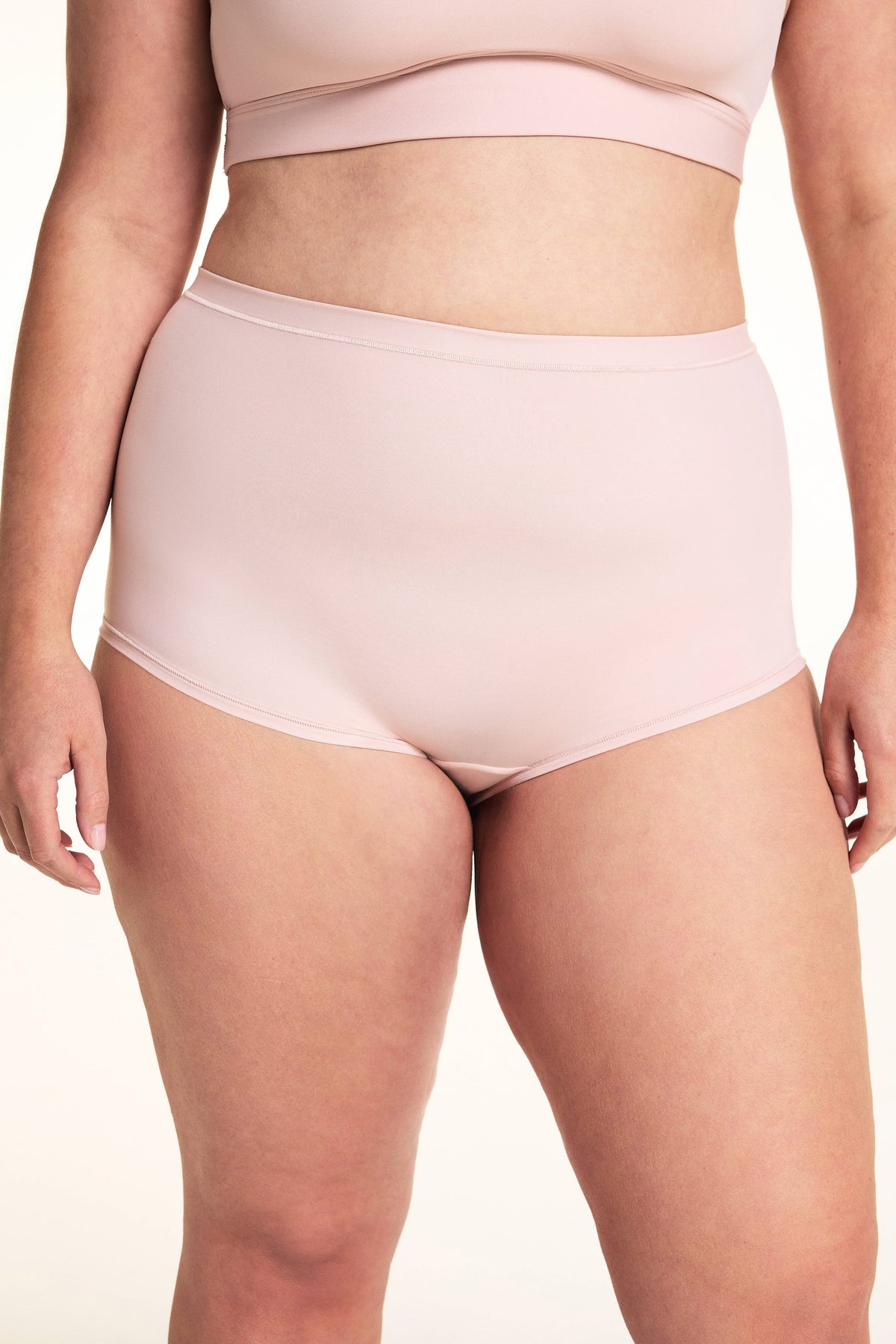 On a light studio backdrop, Alessandra wears the Bliss Boyshort in Ember Rose. The cropped front view highlights the mid-rise waist, full-coverage silhouette, smooth fabric, and soft waistband.