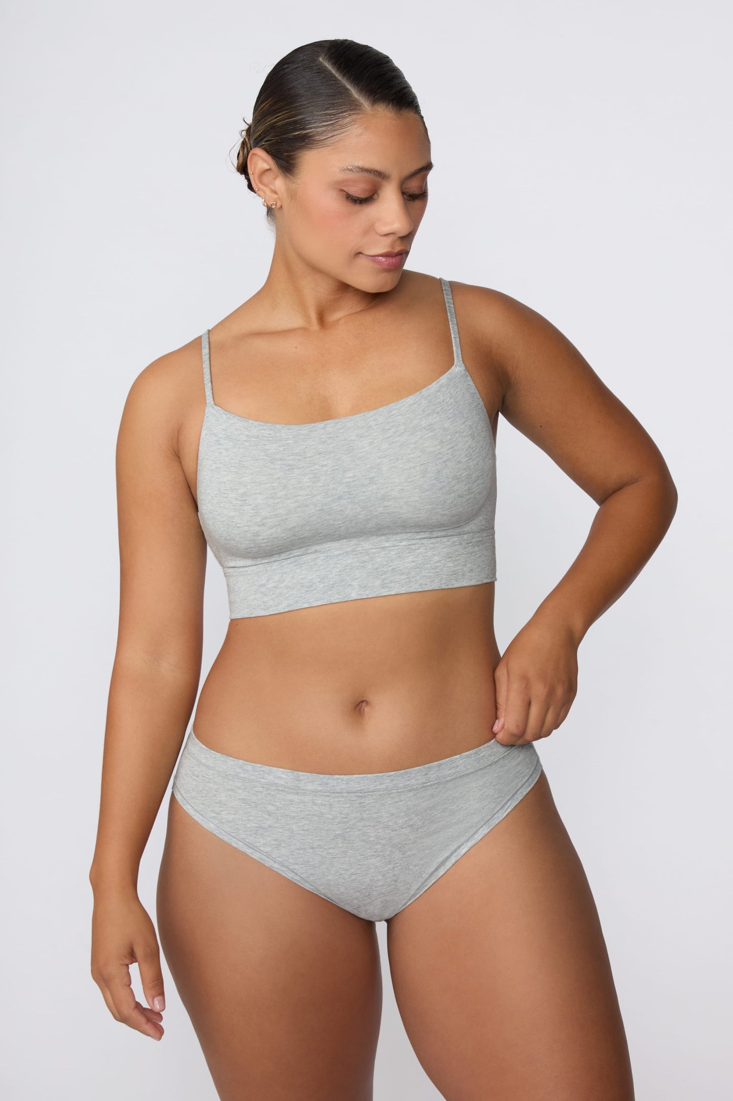 In a studio setting, India wears the Cloud Cotton Thin Strap Bralette in Heather Grey with matching underwear. The front view highlights the straight neckline, thin adjustable straps, and soft cotton fabric.