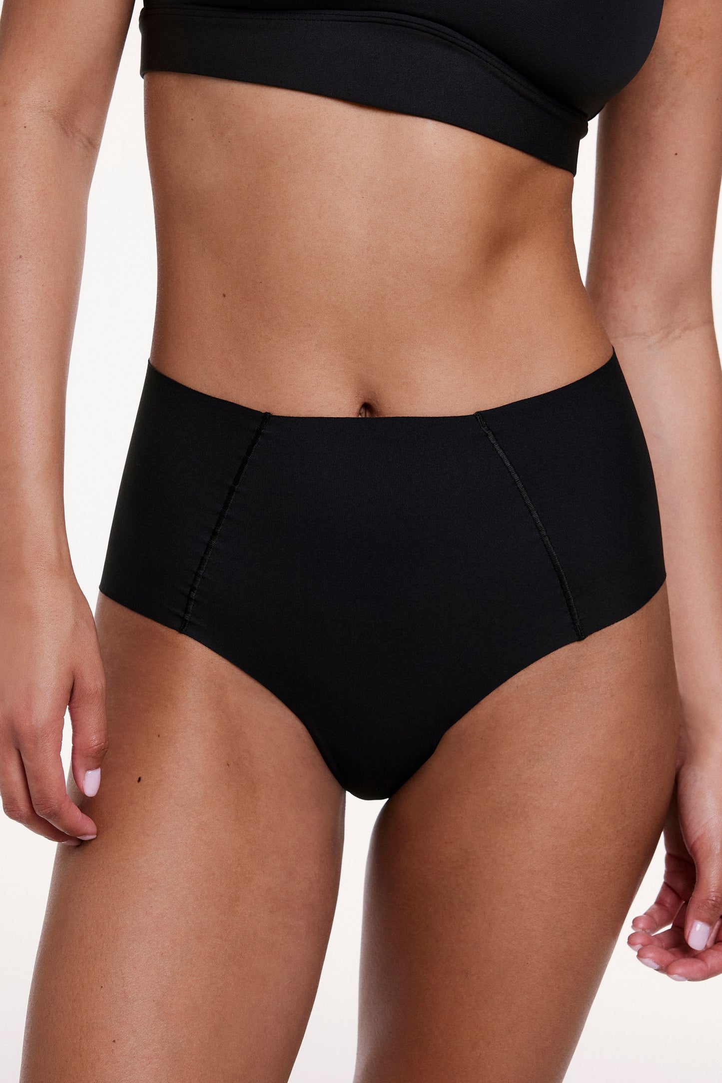 On a white studio backdrop, Courtney wears the No-Show High Waist Brief in Black, shown from the front with a high-rise silhouette and smooth, no-show fabric.