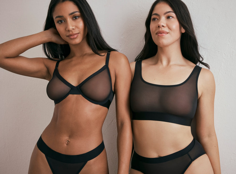 Two models showcasing Harper Wilde's Comfort Mesh collection. On the left, a model wears the ComfortMesh Plunge Bra and matching Thong in Black. On the right, a model wears the Mesh Scoop Bralette and Highwaist Brief in Black. The image highlights the sheer breathable fabric.