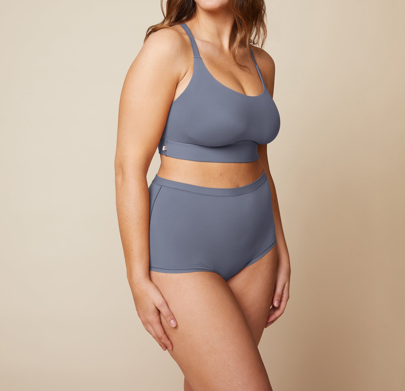 Model standing with her arms down by her side.  She’s wearing the Bliss Racerback Bralette and matching Bliss Boyshort in the color Steel.