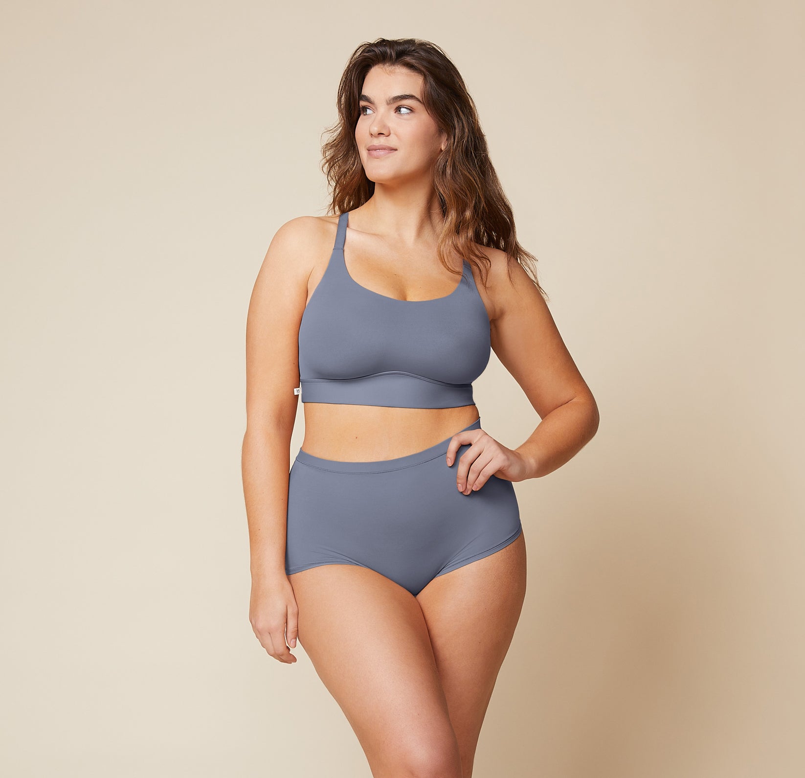 Model standing with her left hand on her hip and her right arm down by her side.  She’s wearing the Bliss Racerback Bralette and matching Bliss Boyshort in the color Steel.