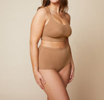 Model standing with her arms down by her side. She’s wearing the Bliss Racerback Bralette and matching Bliss Boyshort in the color Tan.