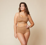 Model standing with her left hand on her hip and her right arm down by her side. She’s wearing the Bliss Racerback Bralette and matching Bliss Boyshort in the color Tan.