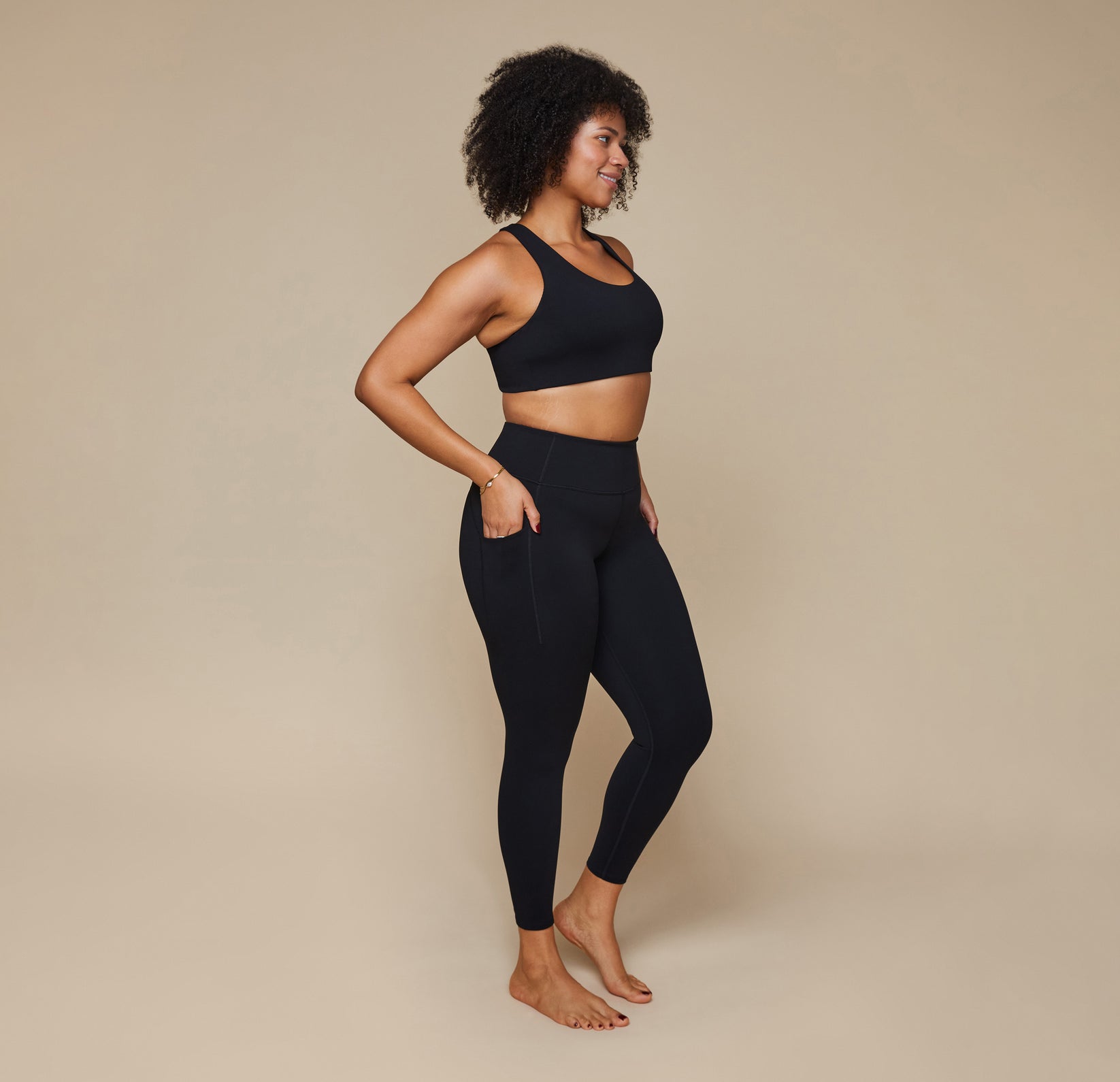 Model wearing the Flex Crossback Convertible Sports Bra and matching Flex High Rise Leggings in Black with her hand in the side pocket of the leggings.