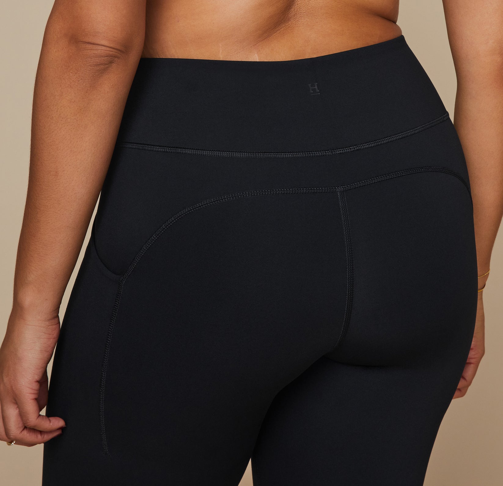 Close up view of the back of the Flex High Rise Leggings in Black showing the small "H" Harper Wilde logo at the top back center of the waistband.