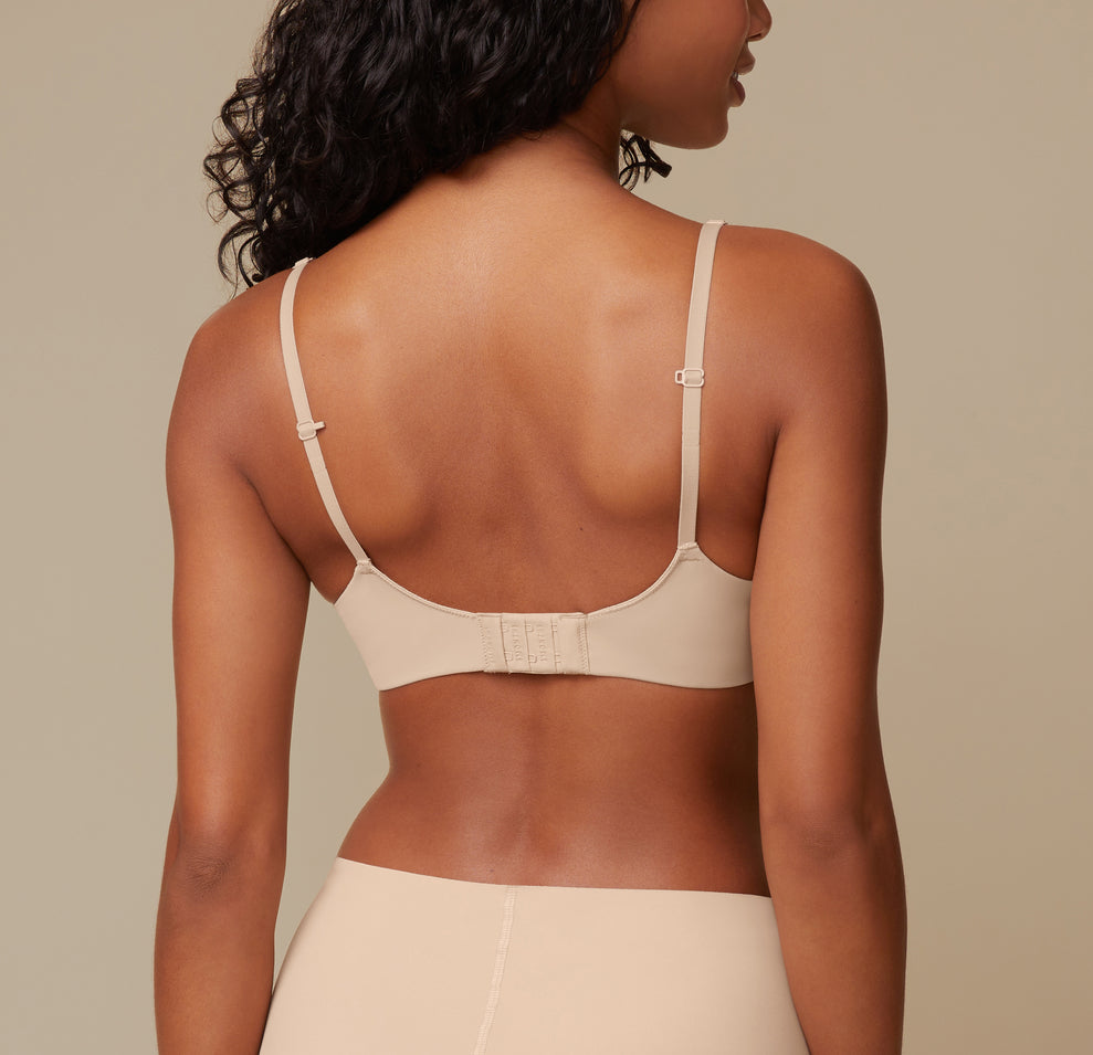 A back view of Ally in the Base Wirefree Bra in Beige, highlighting the ballet back design that offers additional support. The J-hook feature is shown, allowing easy conversion to a racerback.