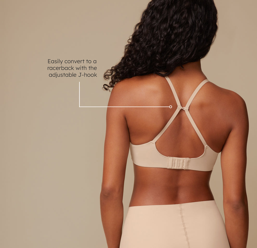 Ally wears the Base Wirefree Bra with the straps converted to a racerback using the J-hook, demonstrating versatility and support for various outfit styles. The tagline reads, "Easily convert to a racerback with the adjustable J-hook."