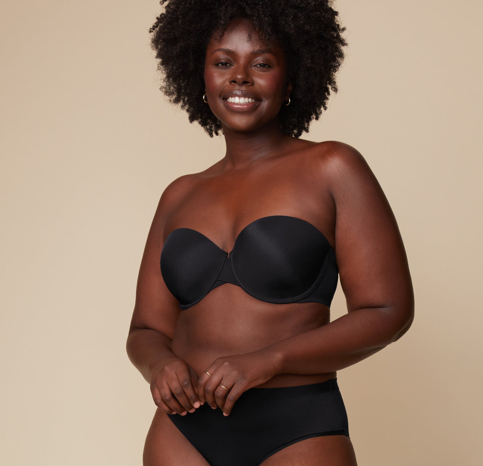 Akesha smiles warmly while wearing the Base Strapless Bra in Black paired with matching high-waist briefs against a neutral backdrop. sizing: Akesha wears size 36D