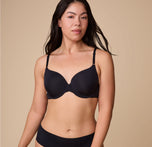 Emersyn models the Base T-Shirt Bra in Black, standing in a relaxed pose to highlight the smooth, form-fitting design. sizing: Emersyn wears size 36C