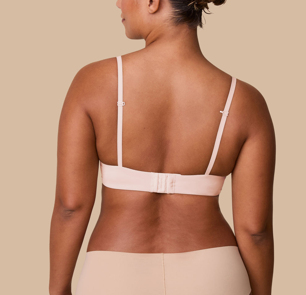 India displays the back of the Base T-Shirt Bra in Rose, highlighting the adjustable hook-and-eye closure and slim, adjustable straps.