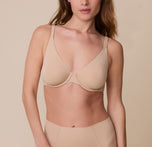 Gracie wears the Base Unlined Bra in Beige, facing forward with a soft expression. The image highlights the unlined, underwire cups and smooth microfiber fabric against a neutral beige background. sizing: Gracie wears 32D