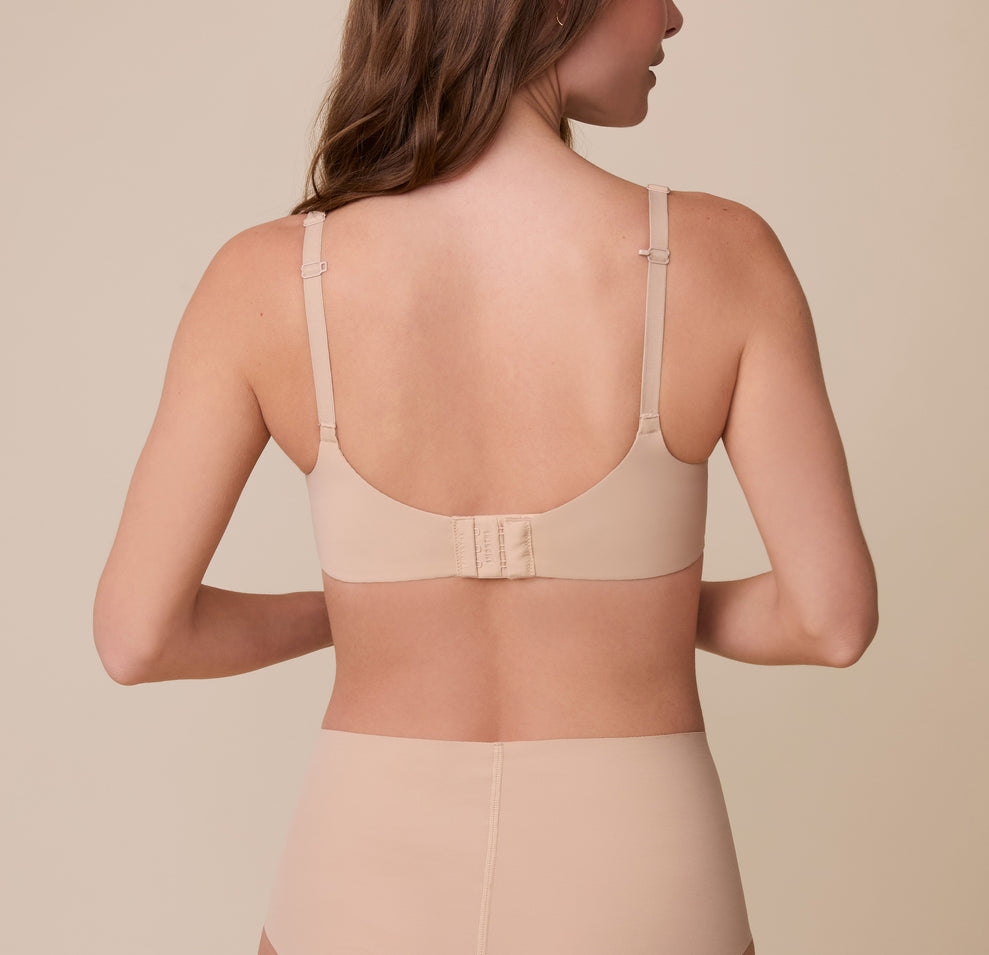 Gracie showcases the back of the Base Unlined Bra in Beige, revealing the wide band, hook-and-eye closure, and convertible racerback feature for a supportive, customizable fit.