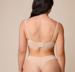 Emersyn faces away from the camera, displaying the back of the Base Unlined Bra in Beige, with its wide, smoothing band, hook-and-eye closure, and convertible racerback feature.