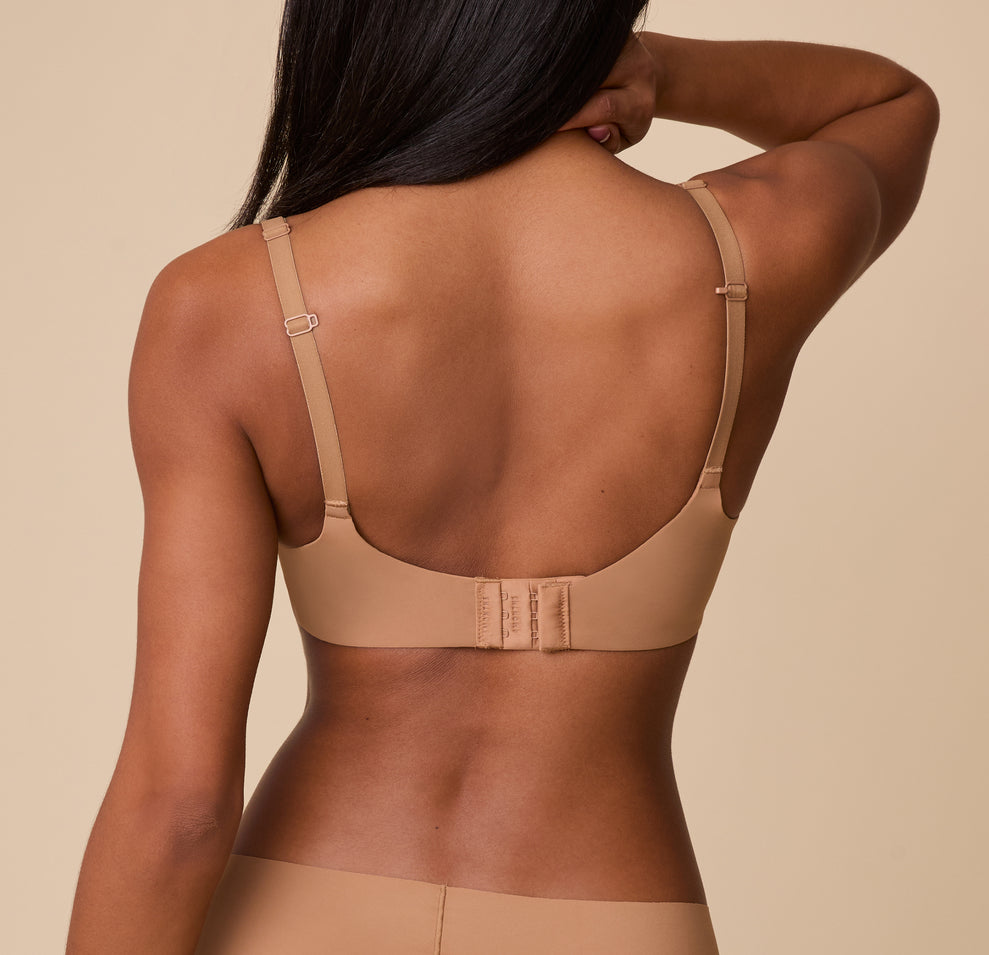 A back view of Ally wearing the Base Unlined Bra in Tan, highlighting the adjustable straps, convertible racerback feature, and hook-and-eye closure for a customizable fit.
