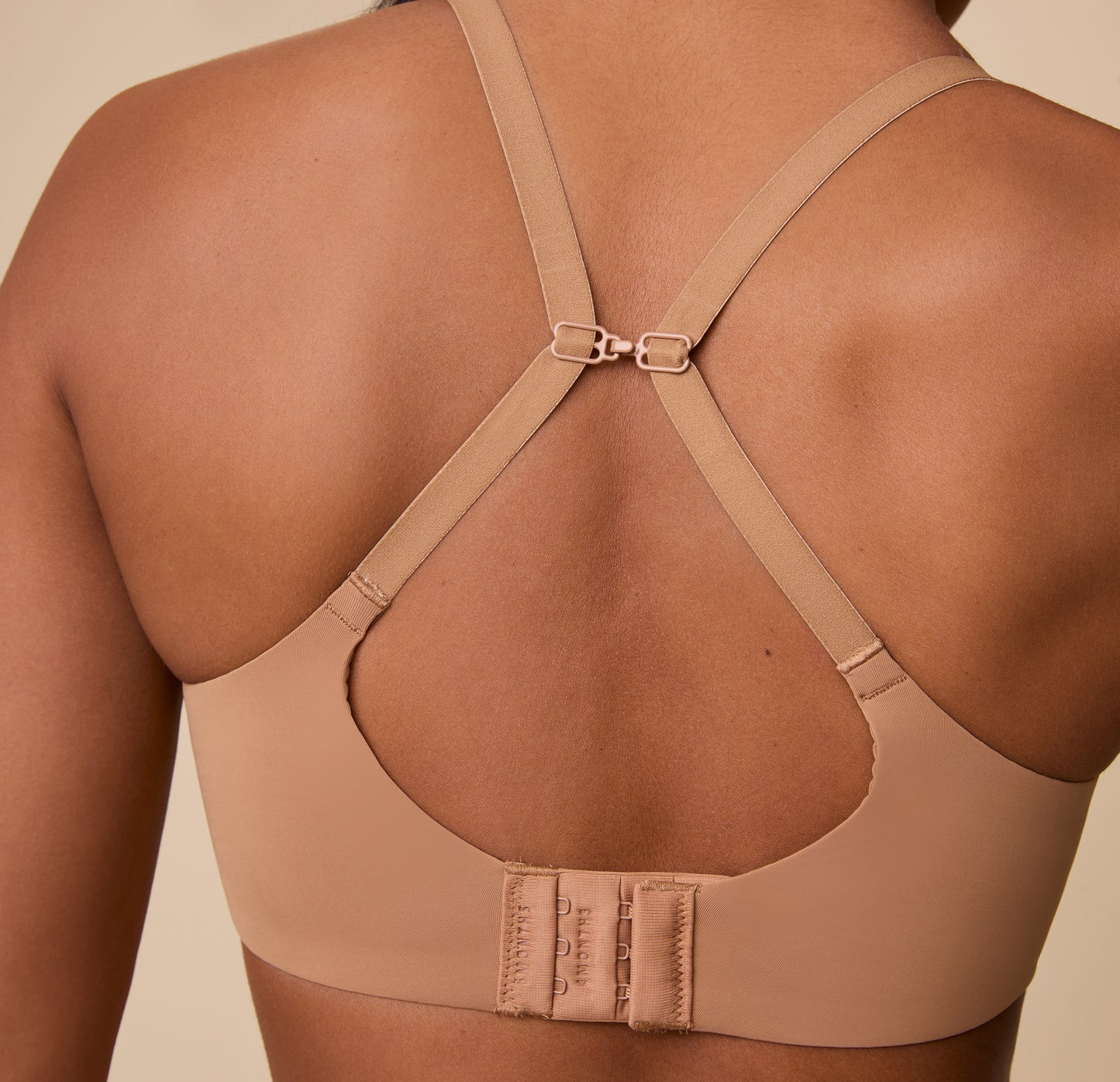 A back view of Ally with the Base Unlined Bra in Tan converted into a racerback style, showcasing the adjustable and versatile straps.