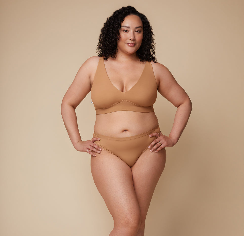 Bianca wearing the Bliss Plunge Adjustable Bralette and Bliss Thong in Tan, facing forward with hands on hips.