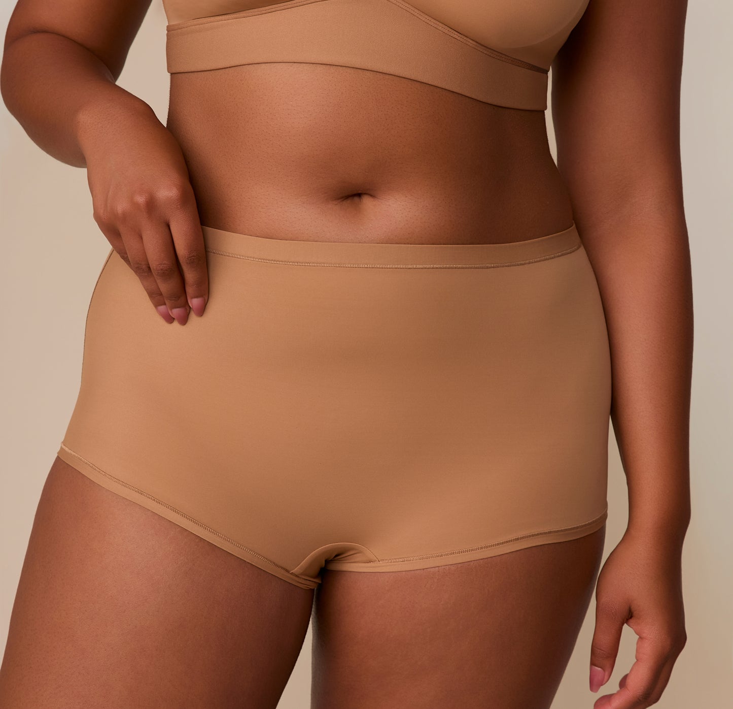Close-up of Zarria adjusting the waistband of the Bliss Boyshort in Tan, highlighting the soft stretch and flat-edge design.