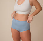 Three quarter view of Sonnie wearing the Bliss Boyshort in Glacier. She adjusts the waistband slightly, highlighting the flexible fit and soft, micro-fiber material.