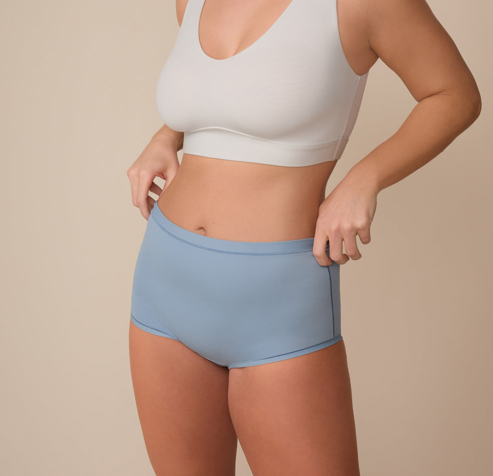 Three quarter view of Sonnie wearing the Bliss Boyshort in Glacier. She adjusts the waistband slightly, highlighting the flexible fit and soft, micro-fiber material.