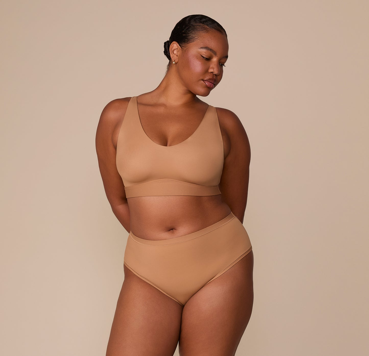 Zarria stands in the full Bliss Bralette and the matching Bliss Highwaist Brief in Tan, demonstrating the minimal seams and all-day comfort.