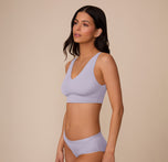 Marcela stands in a three-quarter profile wearing the Bliss Bralette in Violet and Bliss Hiphugger in Violet. The side angle highlights the bralette’s molded shape, supportive underband, and the soft, flexible fit of the hiphugger.