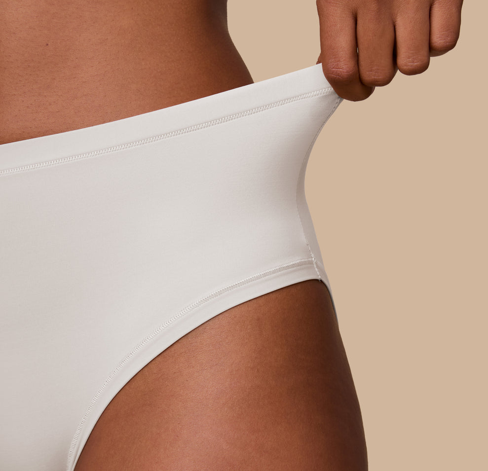 Detail shot of Ally pulling the waistband of the Bliss Highwaist Brief in Frost to show its soft stretch and gentle hold, emphasizing comfort and flexibility.