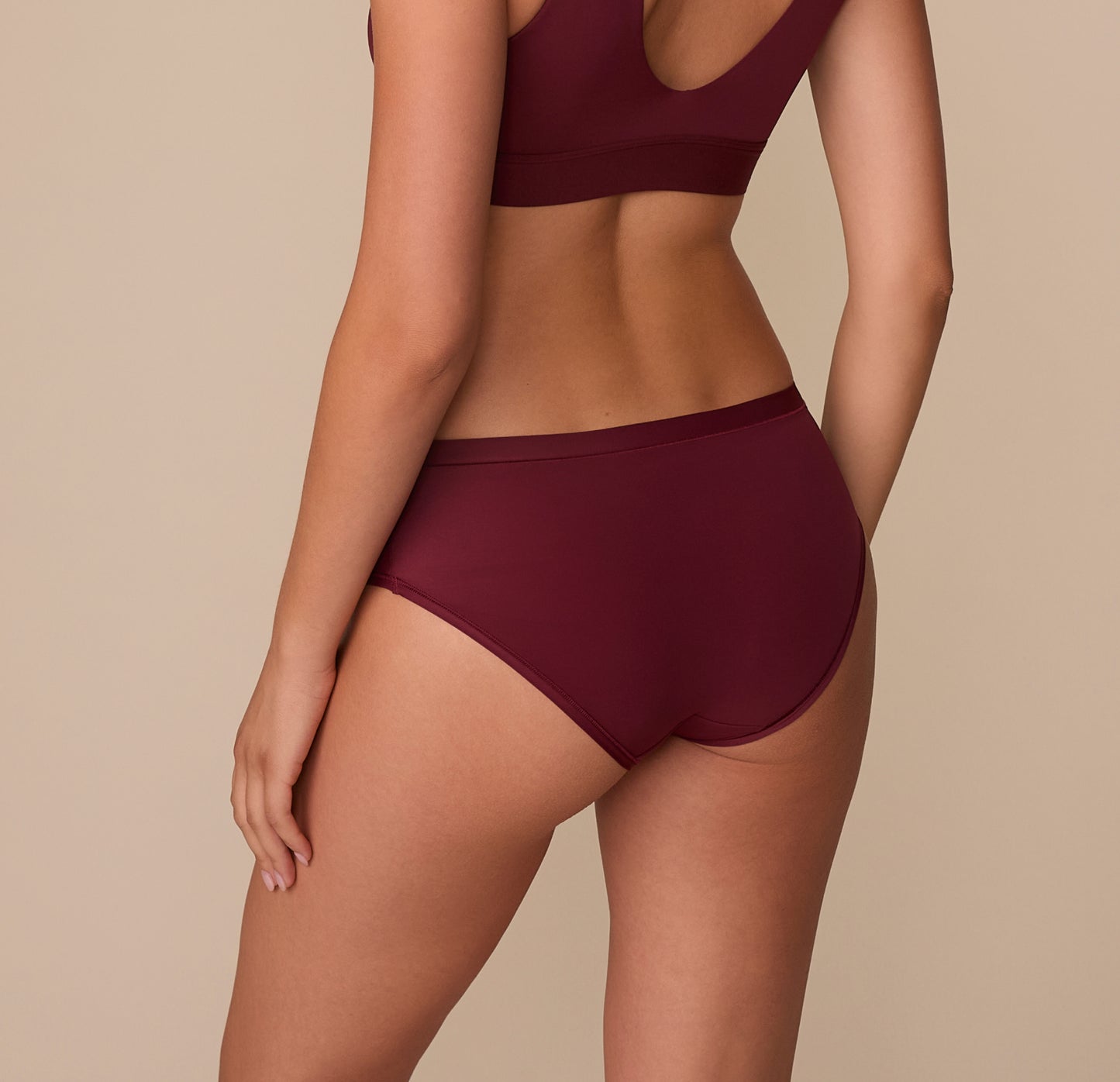 Back view of Alexis in the Bliss Hiphugger in Bordeaux, highlighting the full-coverage design and minimal seam finish across the hips and rear.