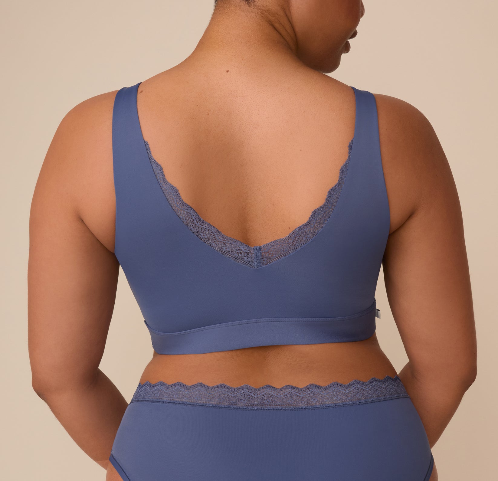 Back view of Zarria in the Bliss Lace Bralette in Twilight. The lace trim detail continues along the deep V-shaped back, emphasizing the minimal seam, supportive band.