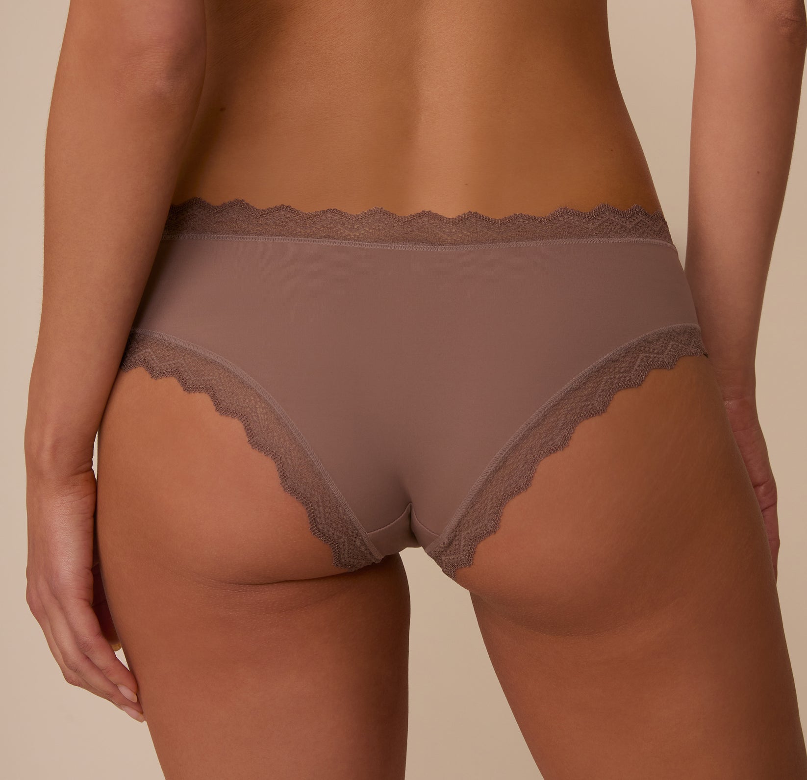 Back angled view of Marcela in the Bliss Lace Cheeky Brief in Mauve, showcasing the brief’s moderate coverage and soft stretch lace that lies flat against the skin.