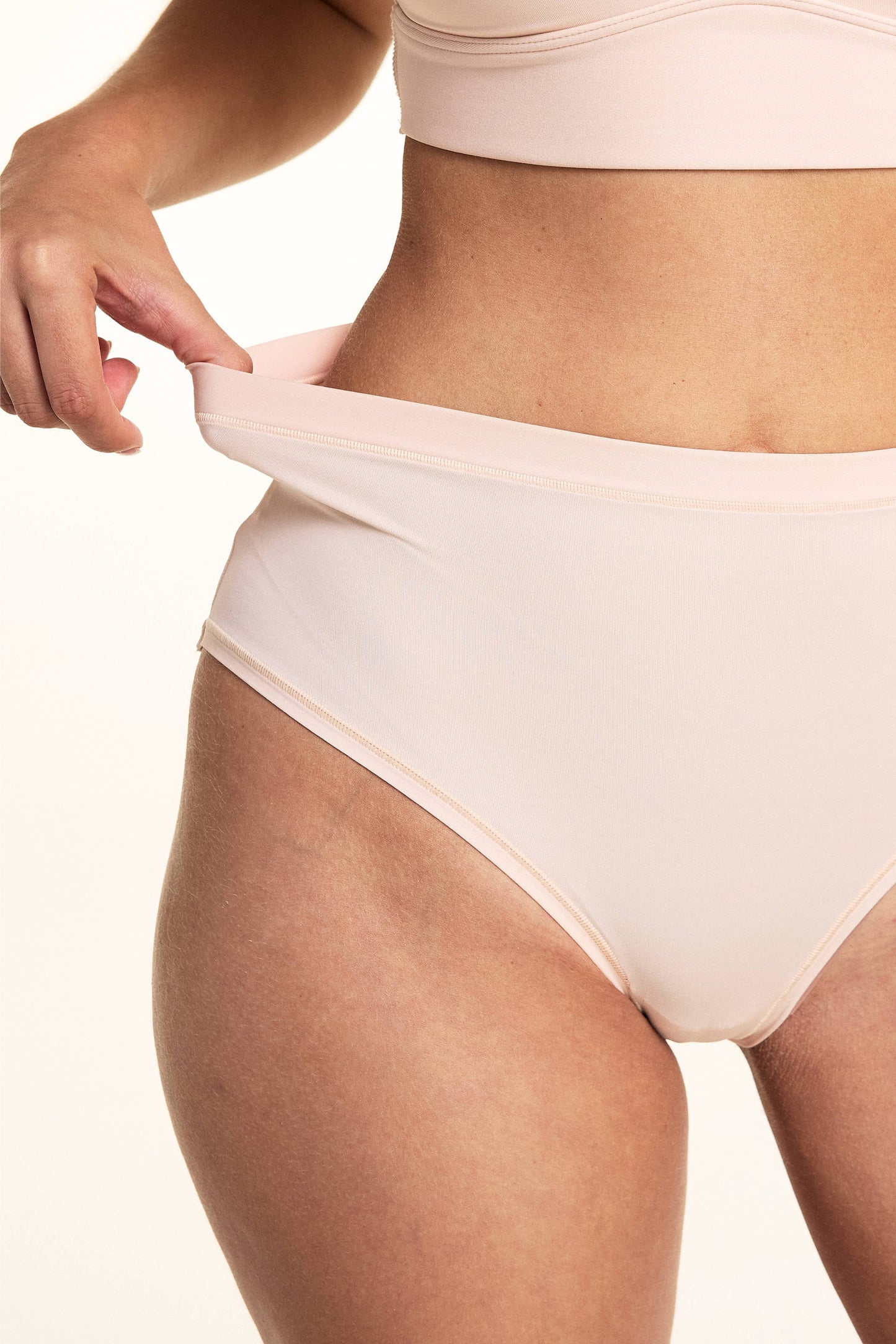 In a studio setting, Laura demonstrates the stretch waistband of the Bliss Lace Highwaist Brief in Rose, featuring smooth microfiber fabric, a high-rise silhouette, and flexible comfort.