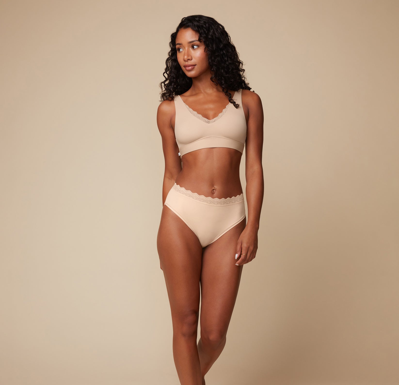 Ally posing in the Bliss Lace Highwaist Brief and matching Bliss Lace Bralette in Beige. The image focuses on the front view, showcasing the lace detailing and smooth fit of both the brief and bralette.