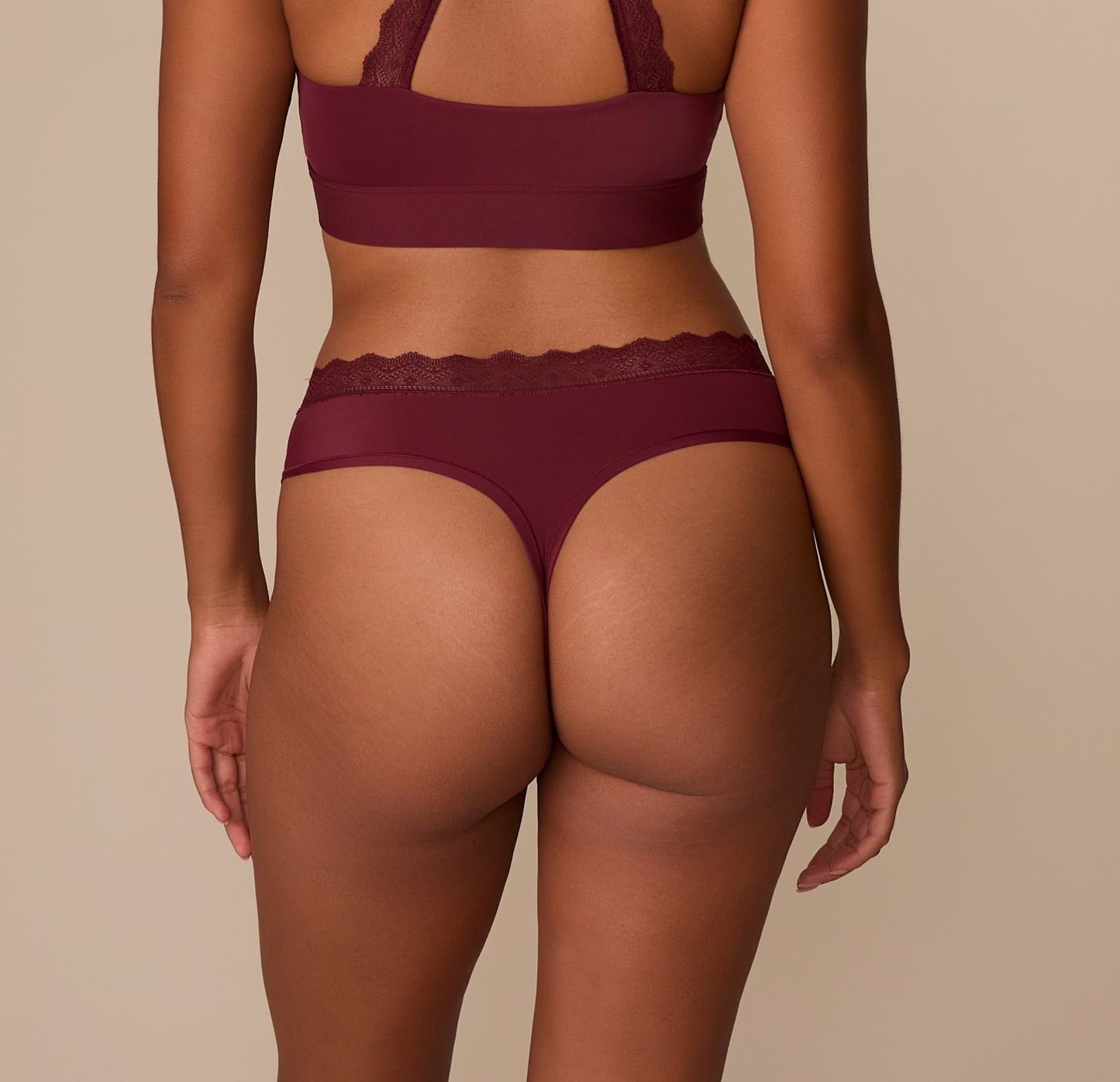 Rear view of Victoria wearing the Bliss Lace Highwaist Thong in Bordeaux. The thong cut offers no back coverage, while the soft lace trim and high waist design deliver support without digging in.