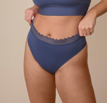 Sonnie adjusting the waistband of the Bliss Lace Highwaist Thong in Twilight. The high-rise waistband is finished with scalloped lace that lays flat without digging in. sizing: Sonnie wears size XL