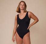Sonnie standing confidently in the Bliss Plunge Bodysuit in Black. The full-body shot shows the bodysuit’s full coverage front and its soft, matte finish.