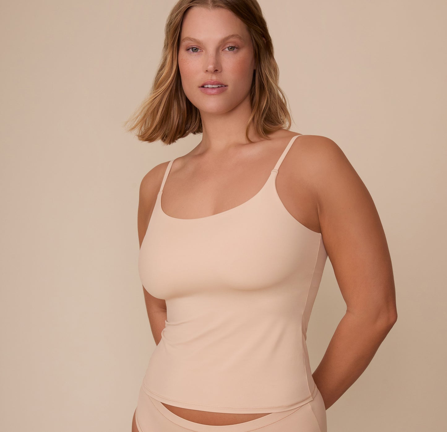 Front view of Sonnie wearing the Bliss Cami in Beige. The cami features a scoop neckline, thin adjustable straps, and a soft, smoothing fit over the torso. sizing: Sonnie wears size Medium