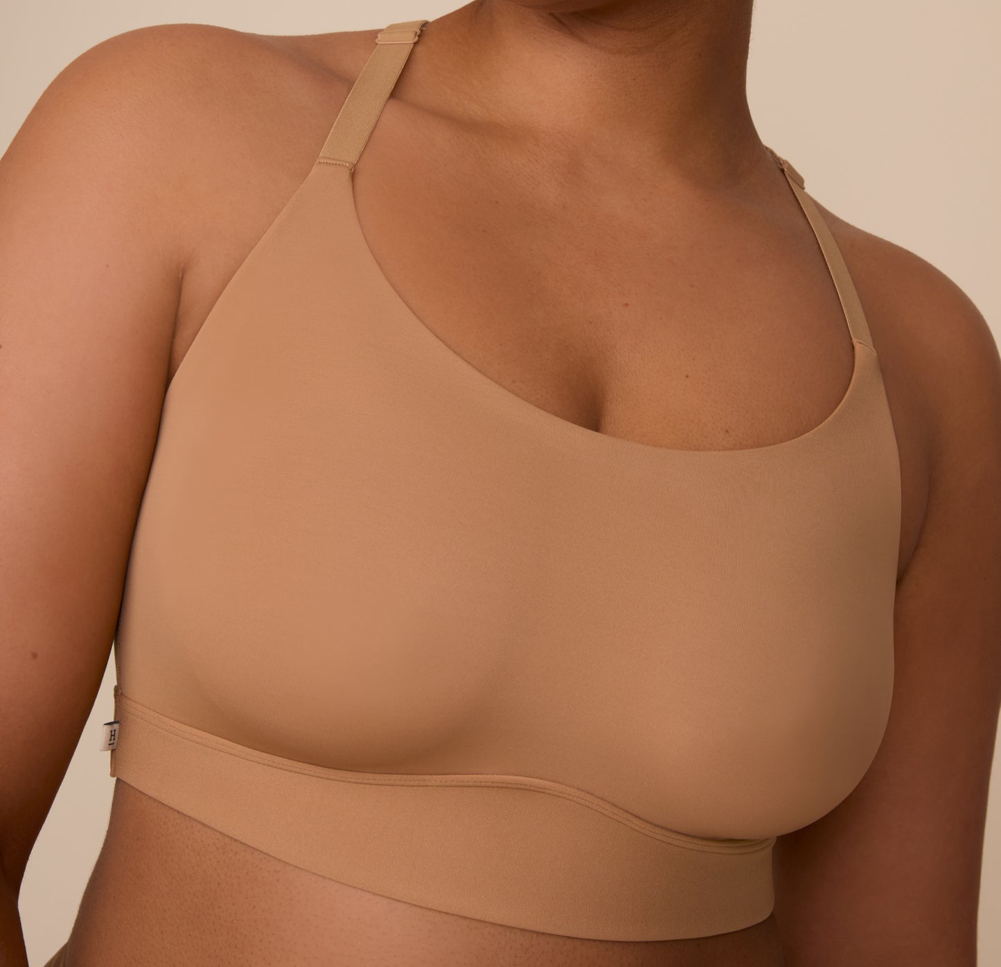 Close up view of Zarria in the Bliss Racerback Bralette in Tan. The outside tag and wide band are emphasized.