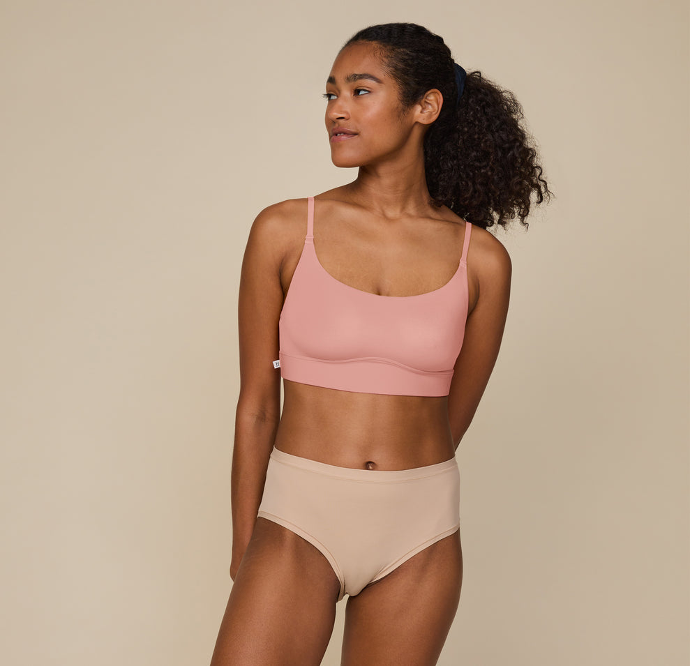 Zoe standing with hands resting at her sides, wearing the Bliss Scoop Bralette in Dusty Rose and the Bliss Highwaist Brief in Beige. She faces forward, smiling softly, showcasing the comfortable fit of both pieces. sizing: Zoe wears size Small