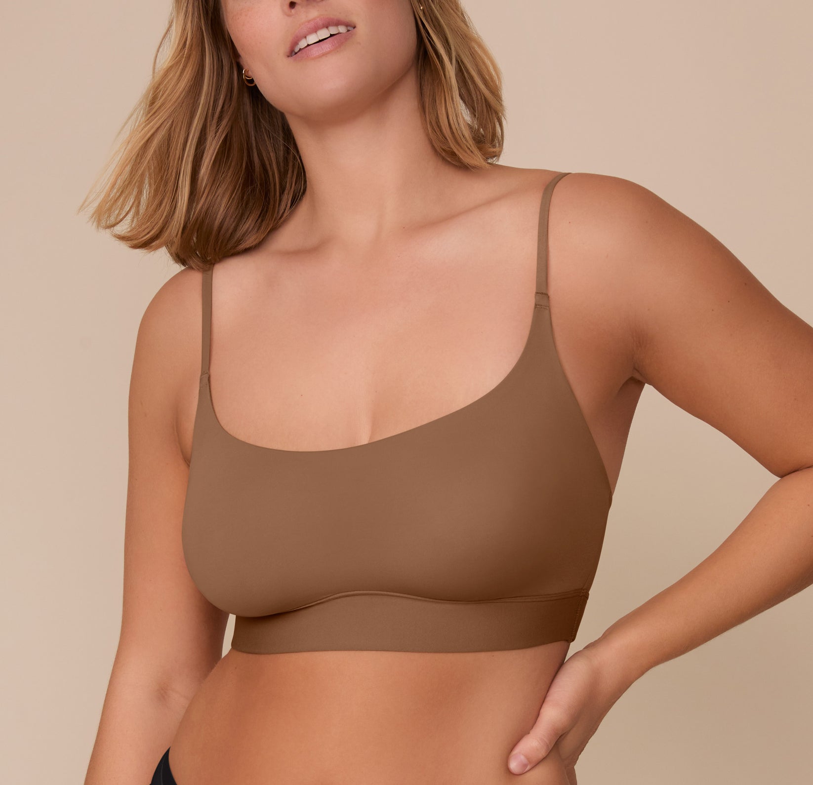 Sonnie facing forward in the Bliss Scoop Bralette in Brown, smiling gently with one hand on her hip. sizing: Sonnie wears size XL