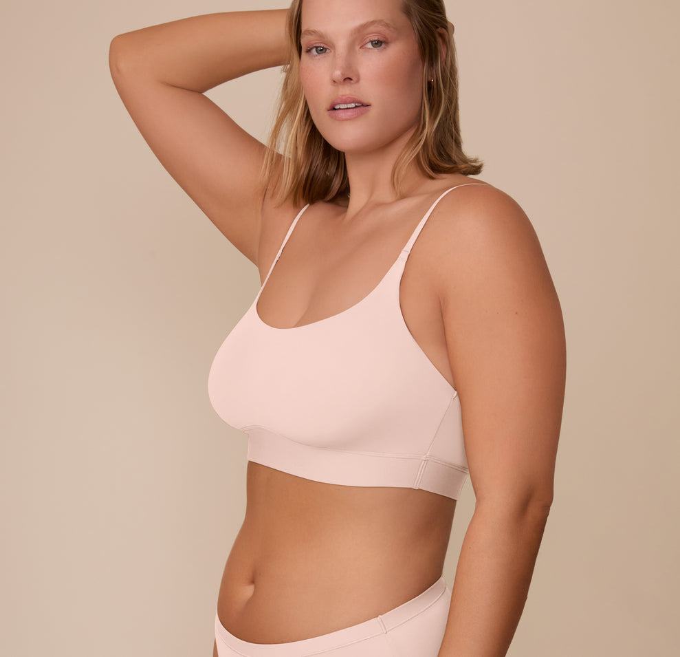 Sonnie models the Bliss Scoop Bralette in Rose from a side profile with one arm lifted, showing the double lined cups and longline band.