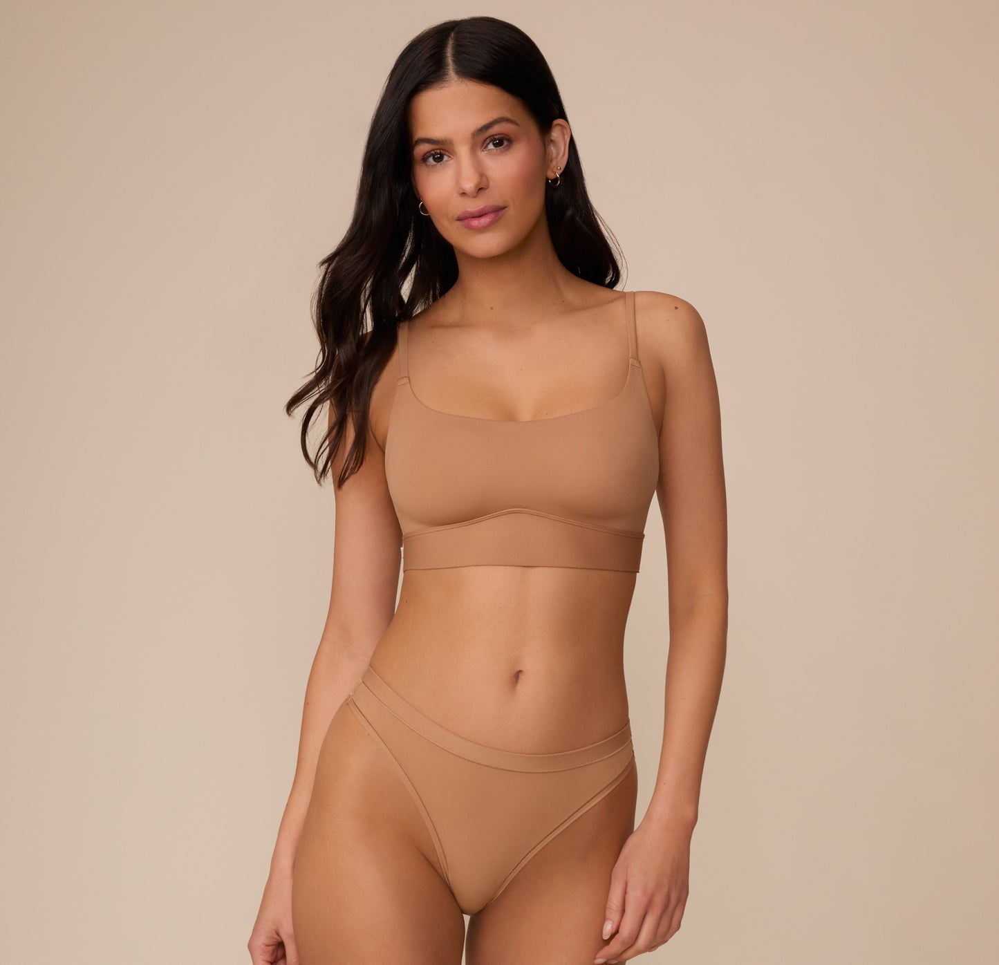 Full body shot of Marcela wearing the Bliss Scoop Bralette in Tan and the matching Bliss Thong, focusing on the soft curve of the bralette's neckline and soft, microfiber texture of the fabric.