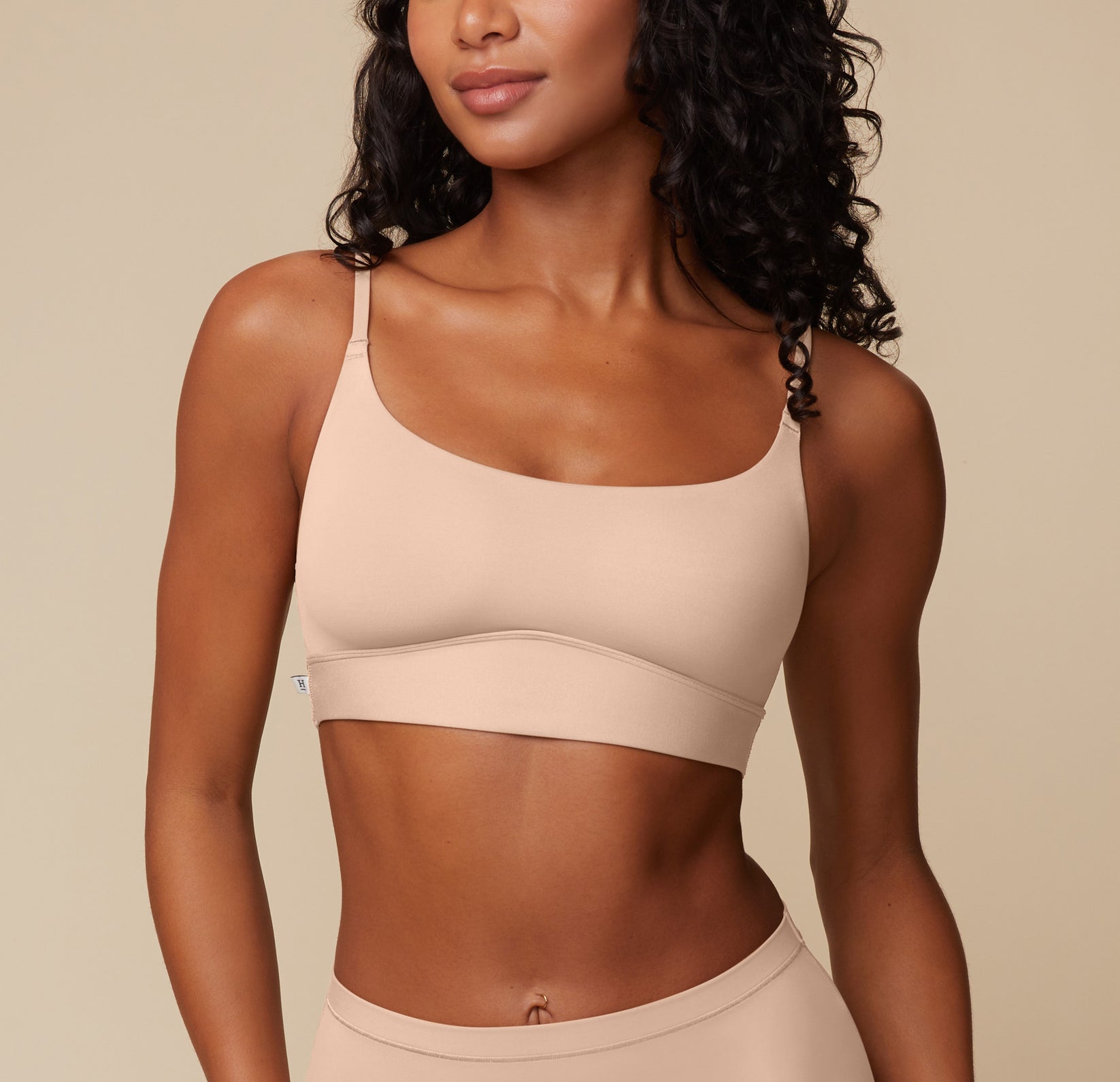 Ally stands smiling softly, wearing the Bliss Scoop Bralette in Beige. The scoop neckline and thin back-adjusting straps are visible, highlighting the bralette’s soft structure and wireless design for everyday comfort. sizing: Ally wears size Small