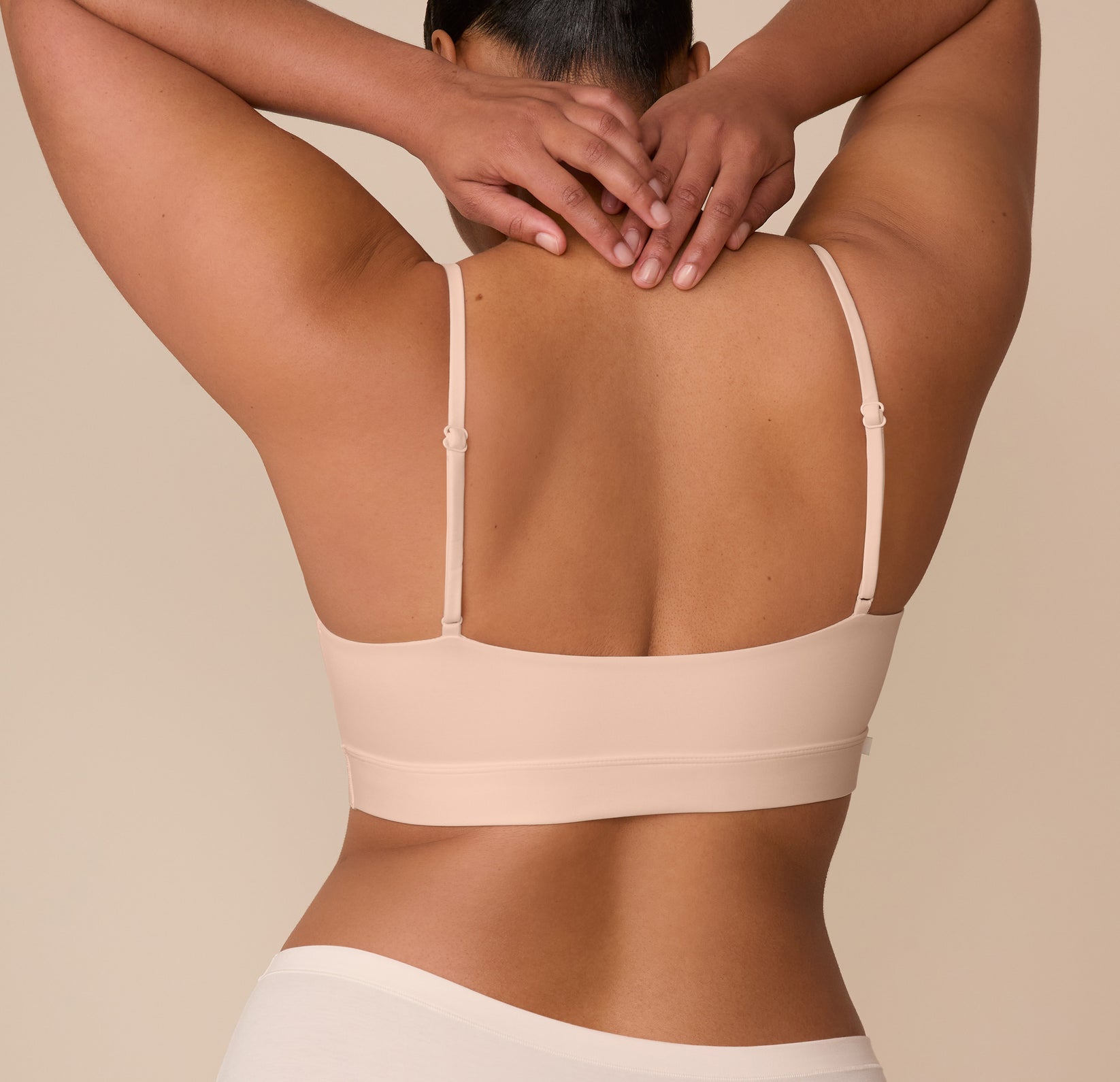 Rear view of Zarria wearing the Bliss Scoop Bralette in Beige, with arms raised to show the back band and adjustable straps.