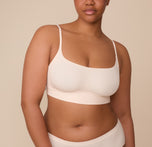 Front view of Zarria wearing the Bliss Scoop Bralette in Quartz. Zarria models the Bliss Scoop Bralette in Quartz. The bralette features a smooth, scoop neckline with slim adjustable straps, offering minimal seam support and everyday comfort. sizing: Zarria wears size XL