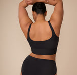 Back view of Zarria raising her arms, highlighting the seamless fit and scoop-back design of the Bliss Square Neck Bralette in Black.