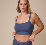 Sonnie wearing the Bliss Square Neck Bralette and Bliss Lace Highwaist Thong in Twilight. She gently adjusts the waistband of the underwear, showcasing the bralette's flattering and supportive silhouette. sizing: Sonnie wears size XL