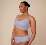 Zarria stands in a side-facing pose wearing a matching Bliss set in Violet, head turned slightly toward the camera. The side profile highlights the Bliss Triangle Bralette’s gentle shaping and wide side band, with the matching Bliss Hiphugger sitting smoothly on her hips.